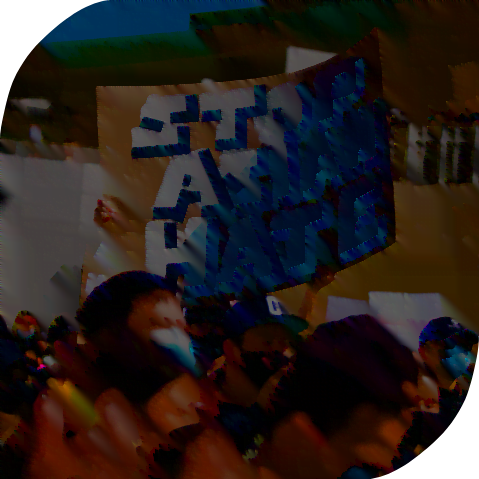 A painted "Stop Asian Hate" cardboard sign being held anonymously in a blurred out crowd in front of a building.
